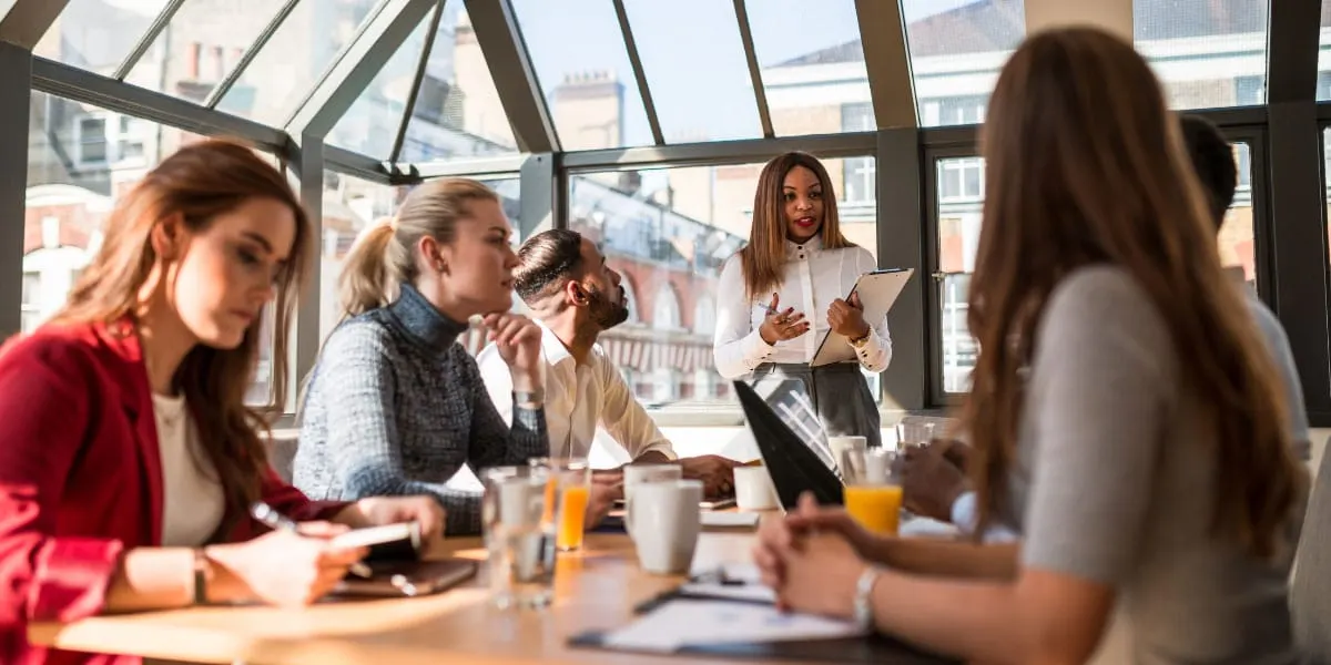 Une dirigeante échange avec son équipe réunie autour d’une table, dans une salle lumineuse
