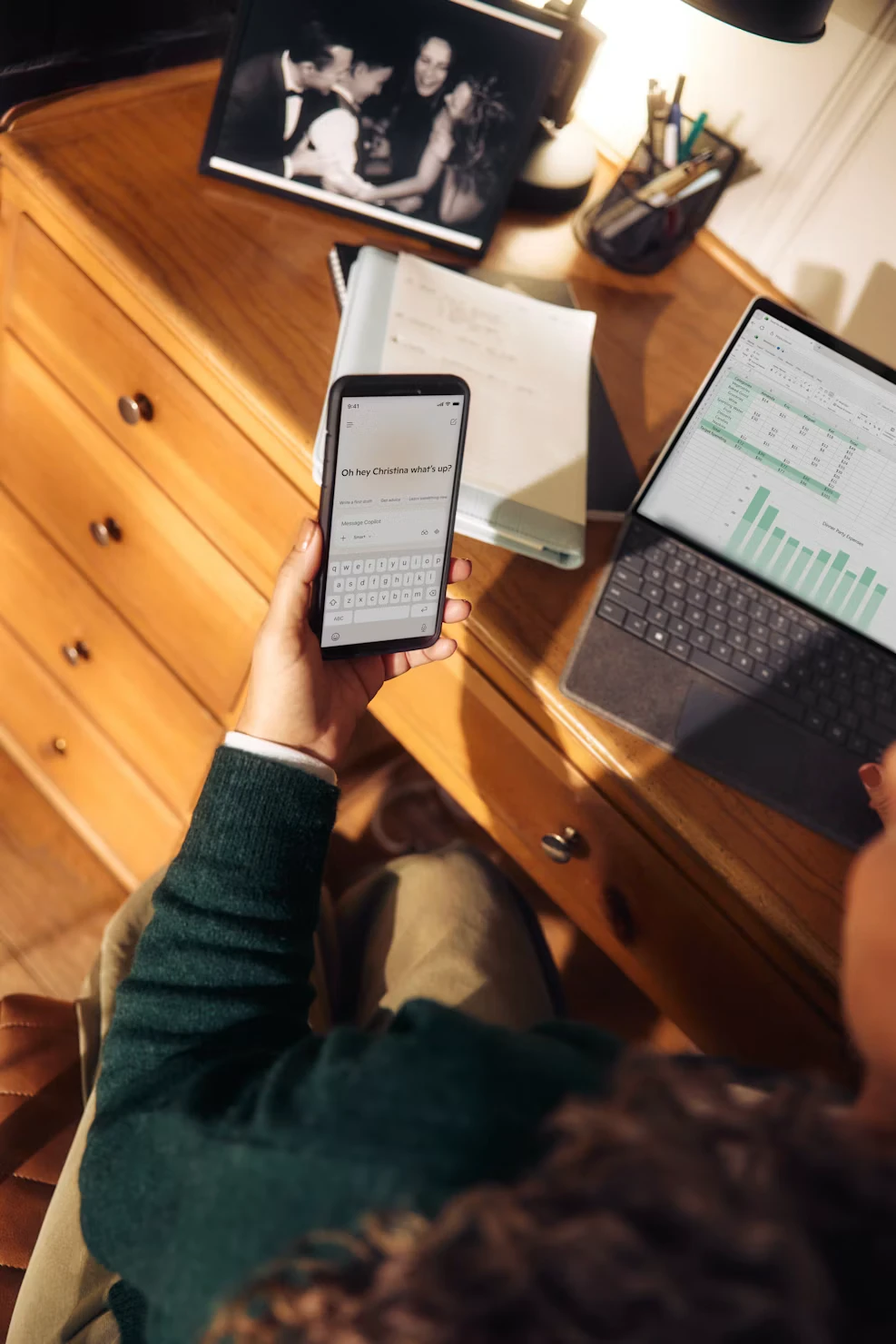 Une collaboratrice utilise un assistant IA sur son téléphone à son poste de travail, un ordinateur portable ouvert à côté